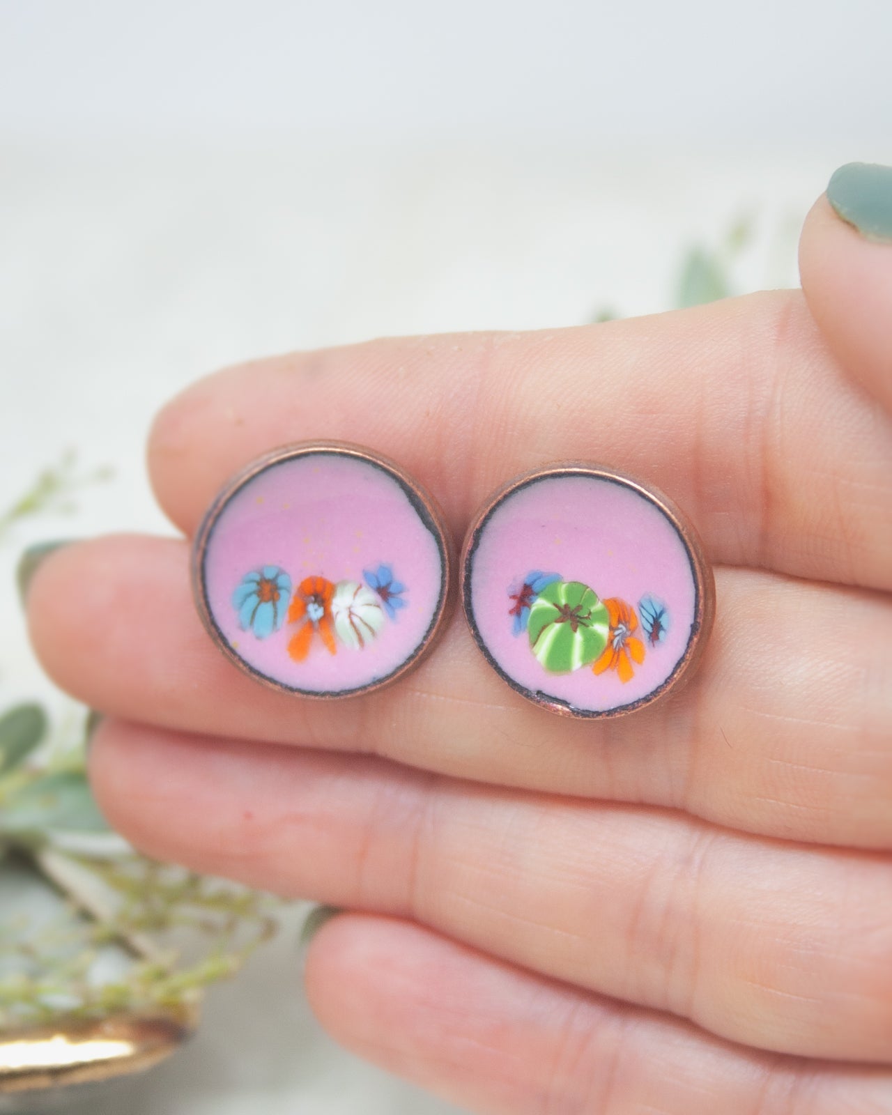 A hand holding two circular earrings with colorful floral designs on them.