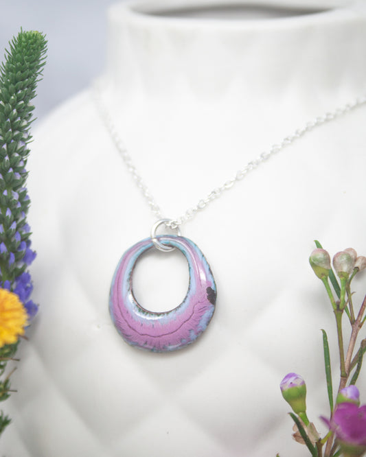 A necklace with a colorful pendant is displayed on a white vase, surrounded by flowers.