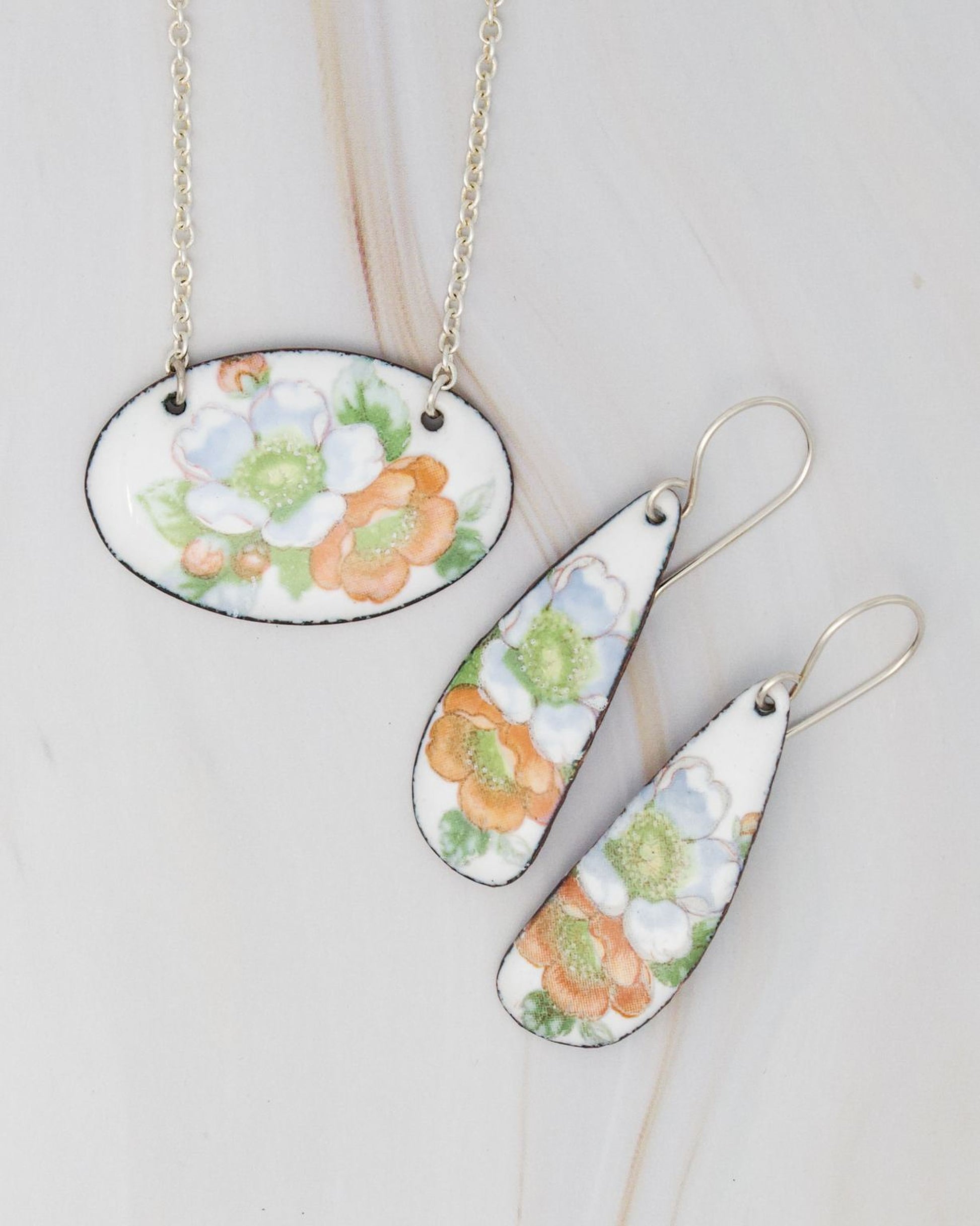 a necklace and earrings with floral designs, including orange and white flowers, on a white background.
