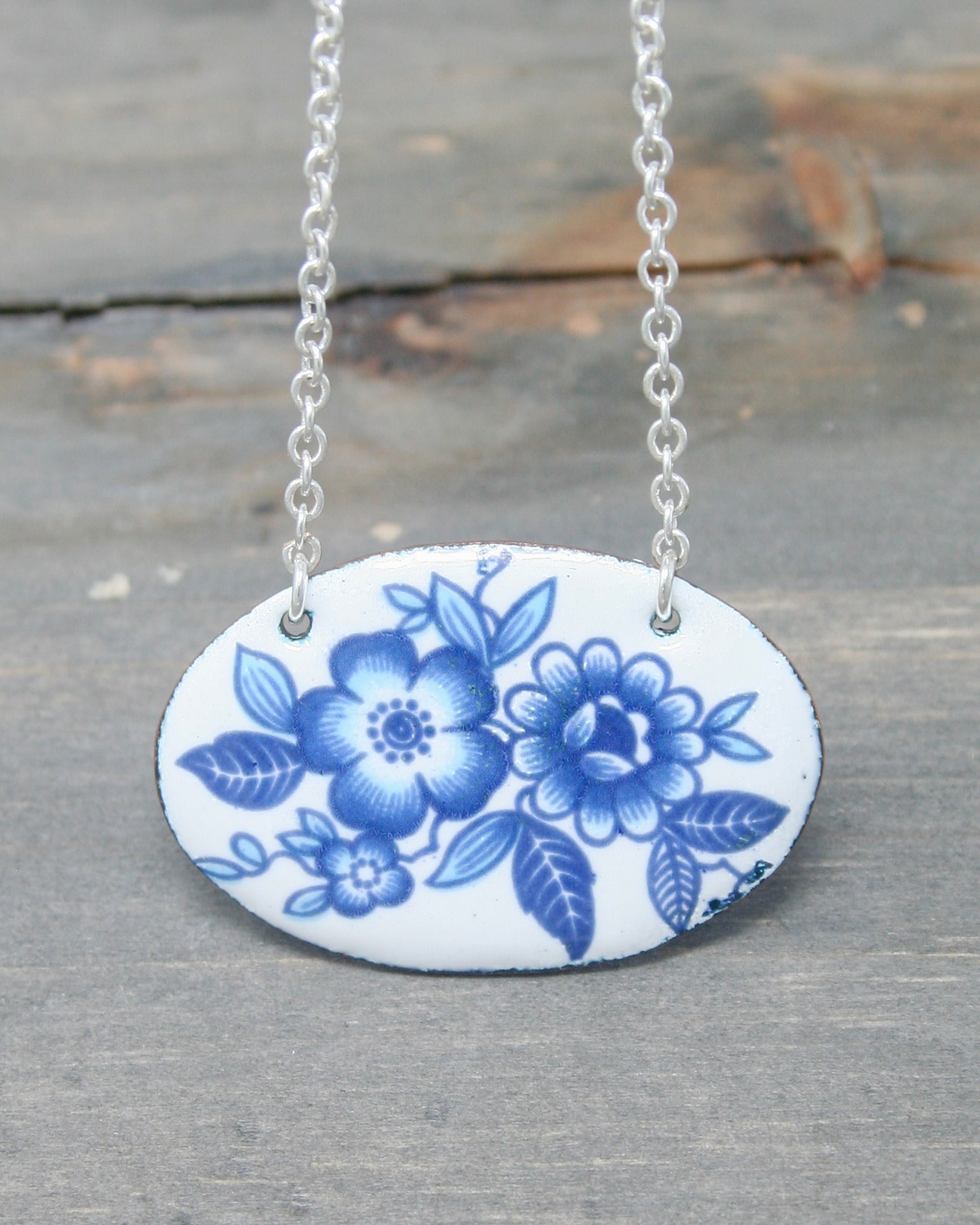 a blue and white flowered ceramic pendant on a chain