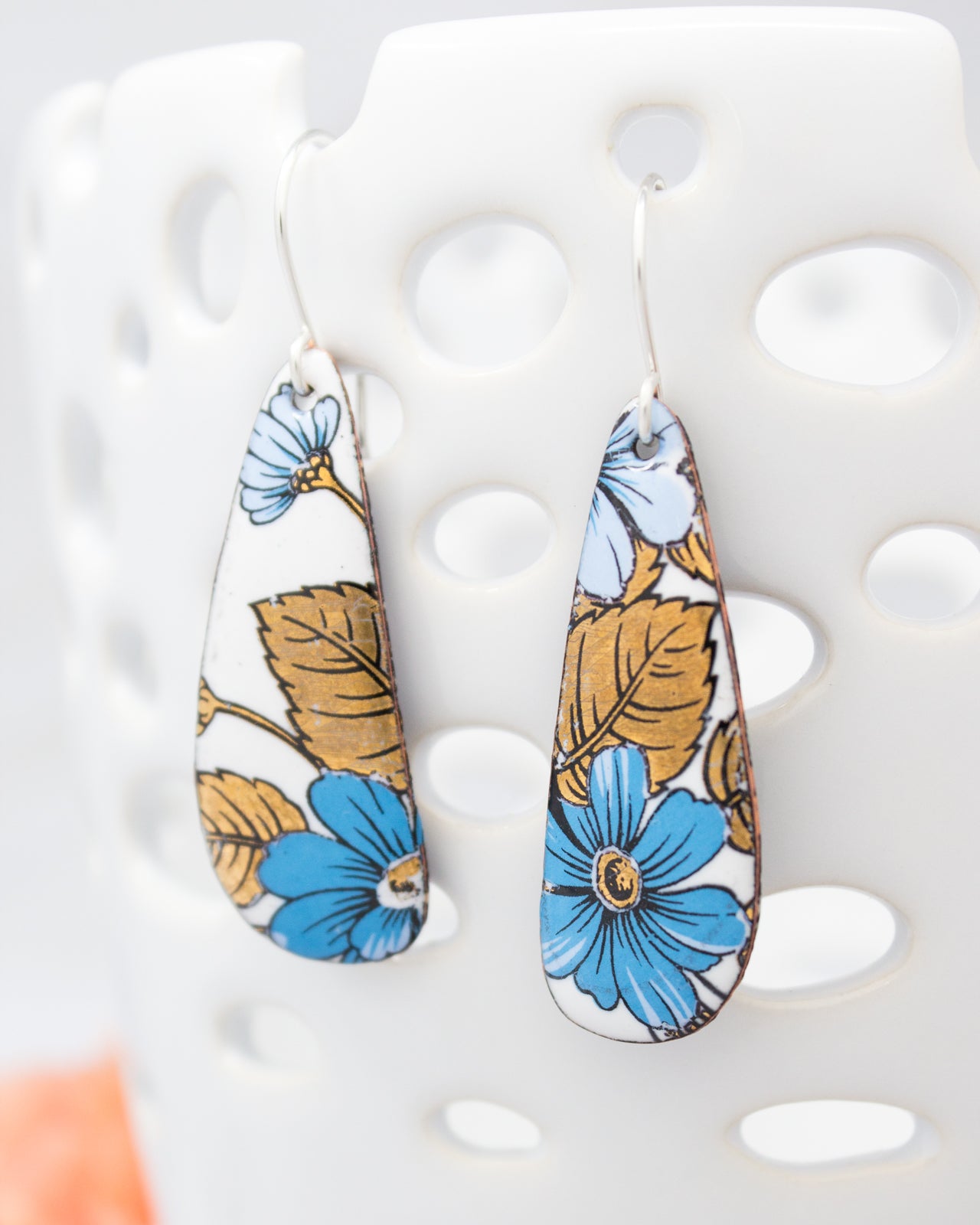 A pair of earrings with a floral design, featuring blue and orange flowers on a white background.