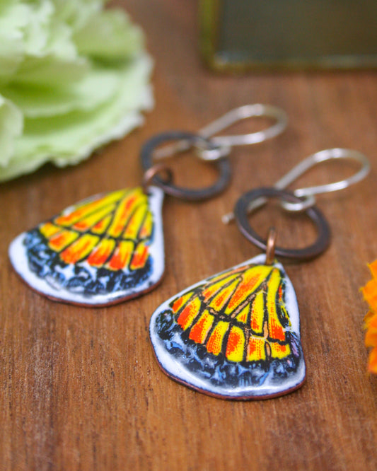 a pair of colorful earrings with butterfly-like designs, placed on a wooden surface.