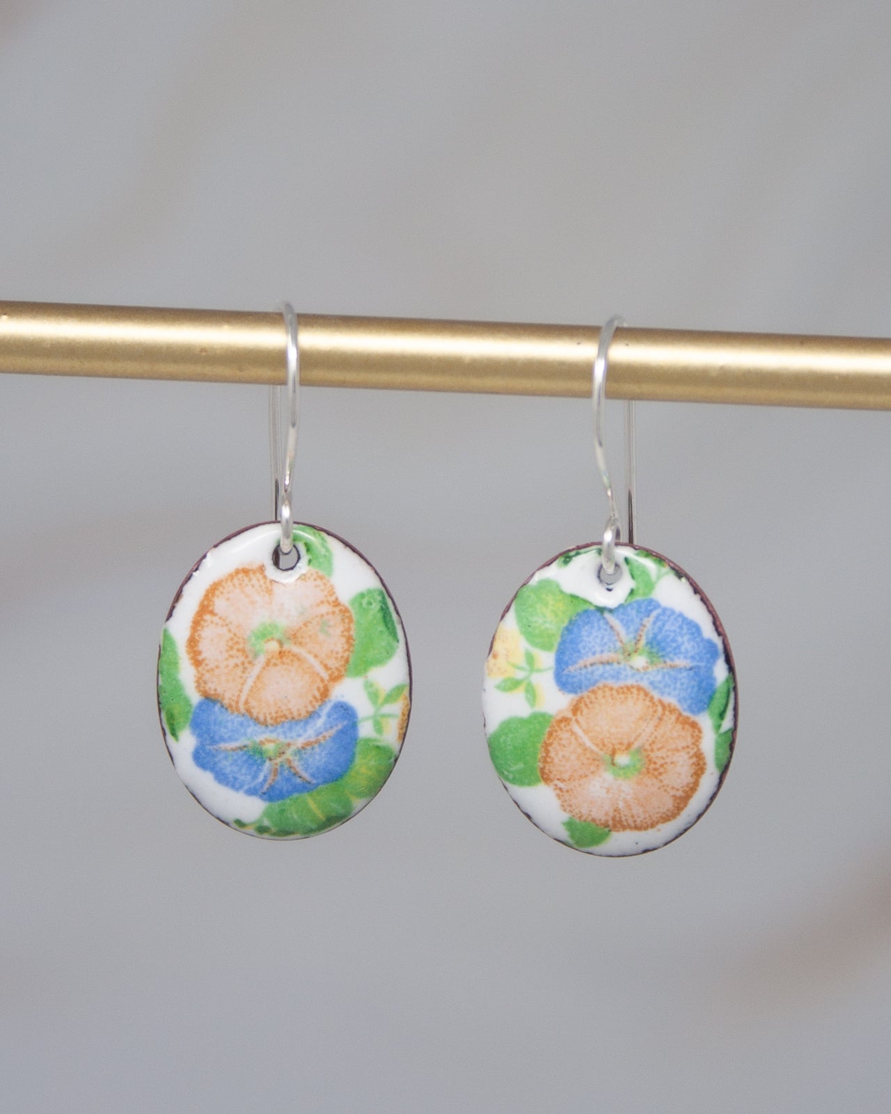 A pair of earrings with a floral design, featuring blue and orange flowers on a white background.