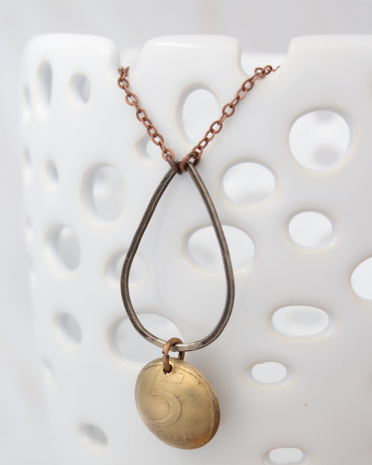 A gold-colored pendant with the number 5 on it, hanging from a chain against a white background.