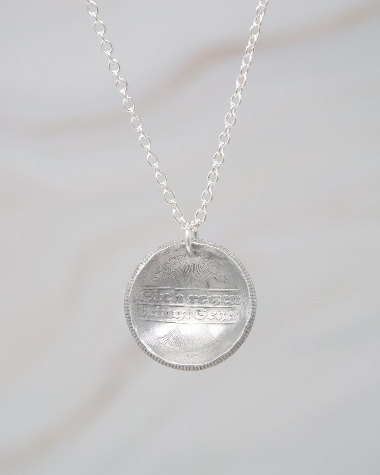 A silver necklace with a pendant featuring an engraved design.