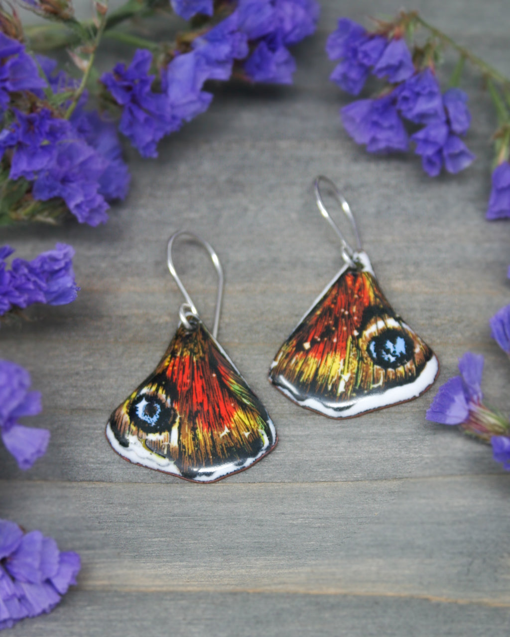 a close up of a pair of earrings near purple flowers