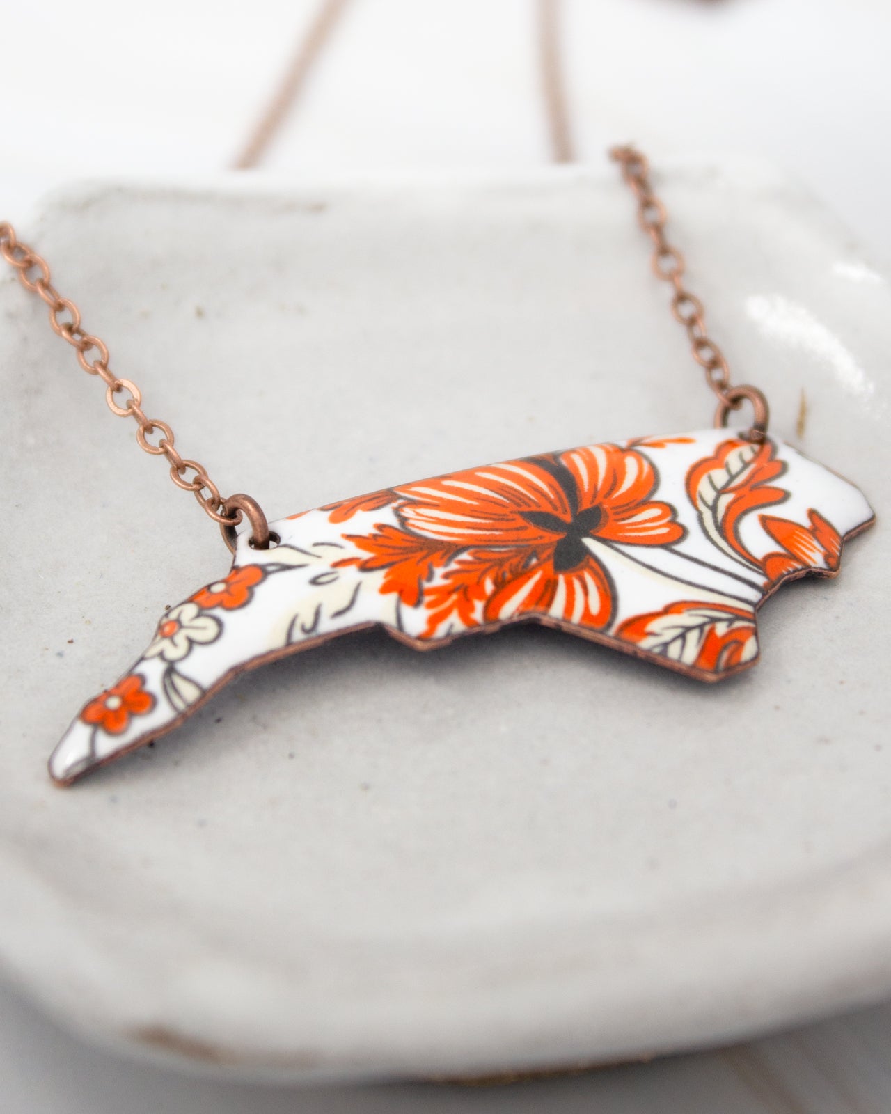 A necklace with a pendant in the shape of a flower design, featuring orange and white colors.