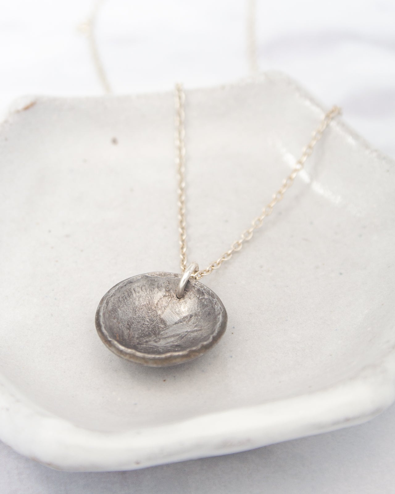 A silver necklace with a pendant is displayed on a white plate.