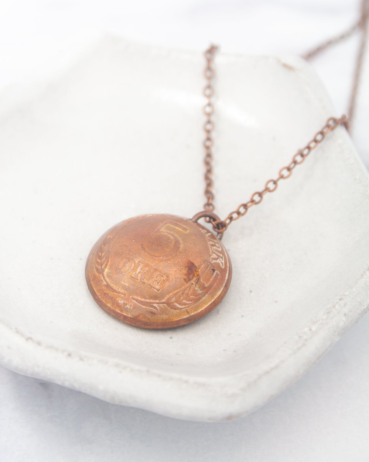 A copper-colored coin pendant necklace with the number 5 on it, resting on a white surface.