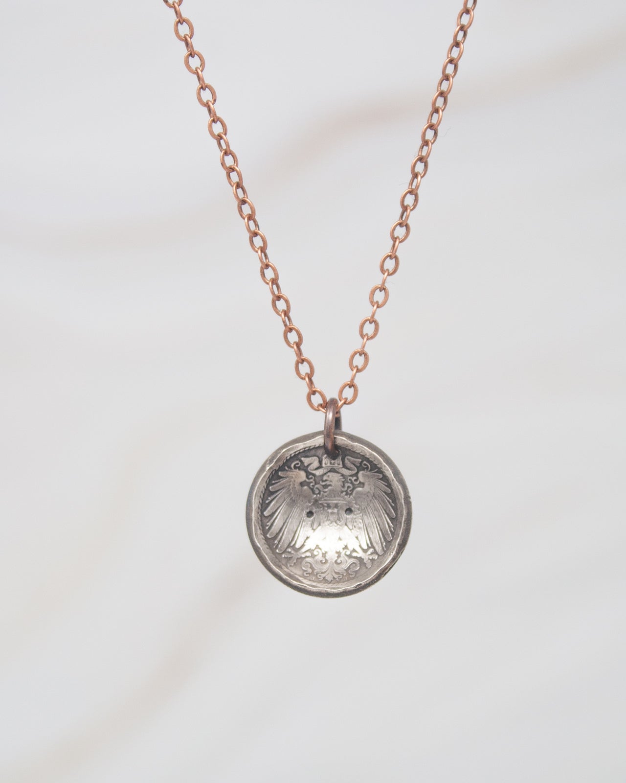 A silver-colored pendant necklace with a circular pendant featuring an intricate design.