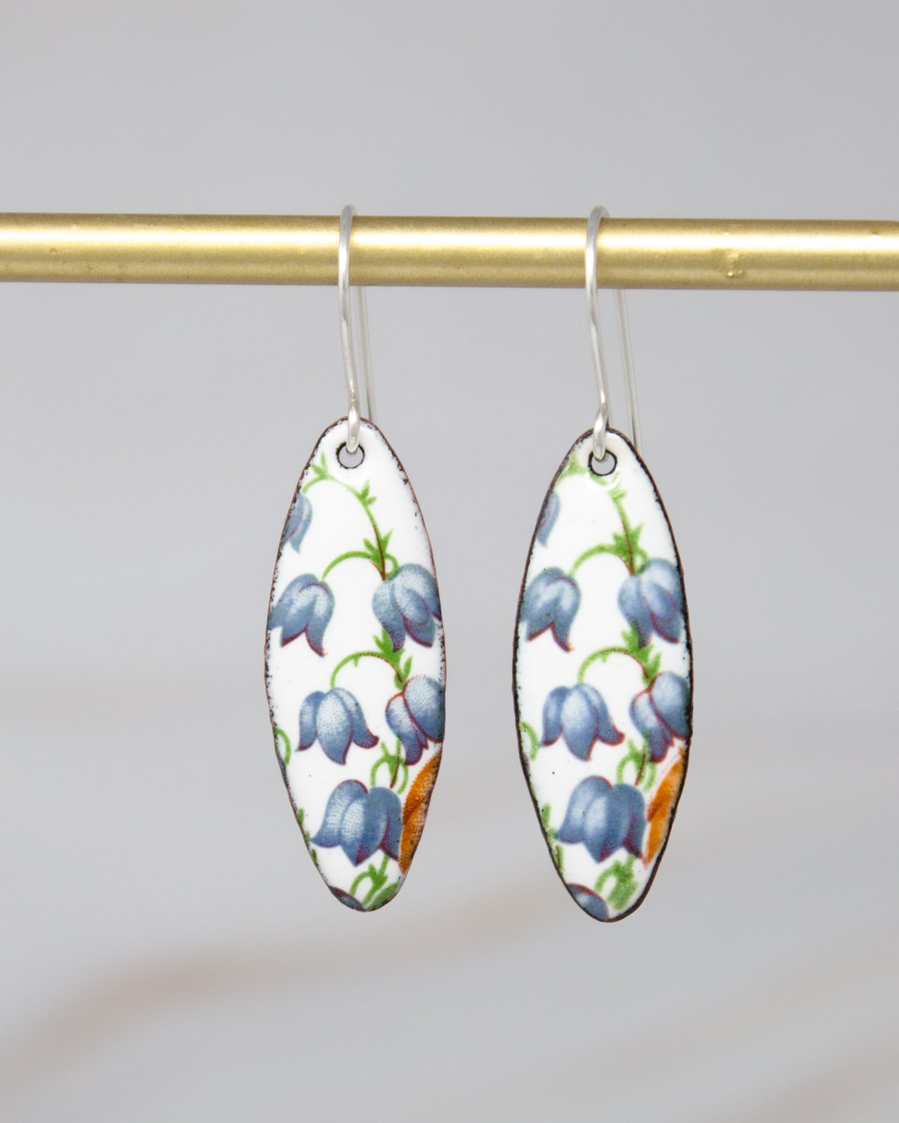 A pair of earrings with a floral pattern on a white background, hanging from a gold bar.
