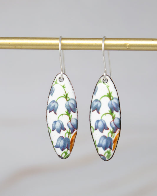 A pair of earrings with a floral pattern on a white background, hanging from a gold bar.