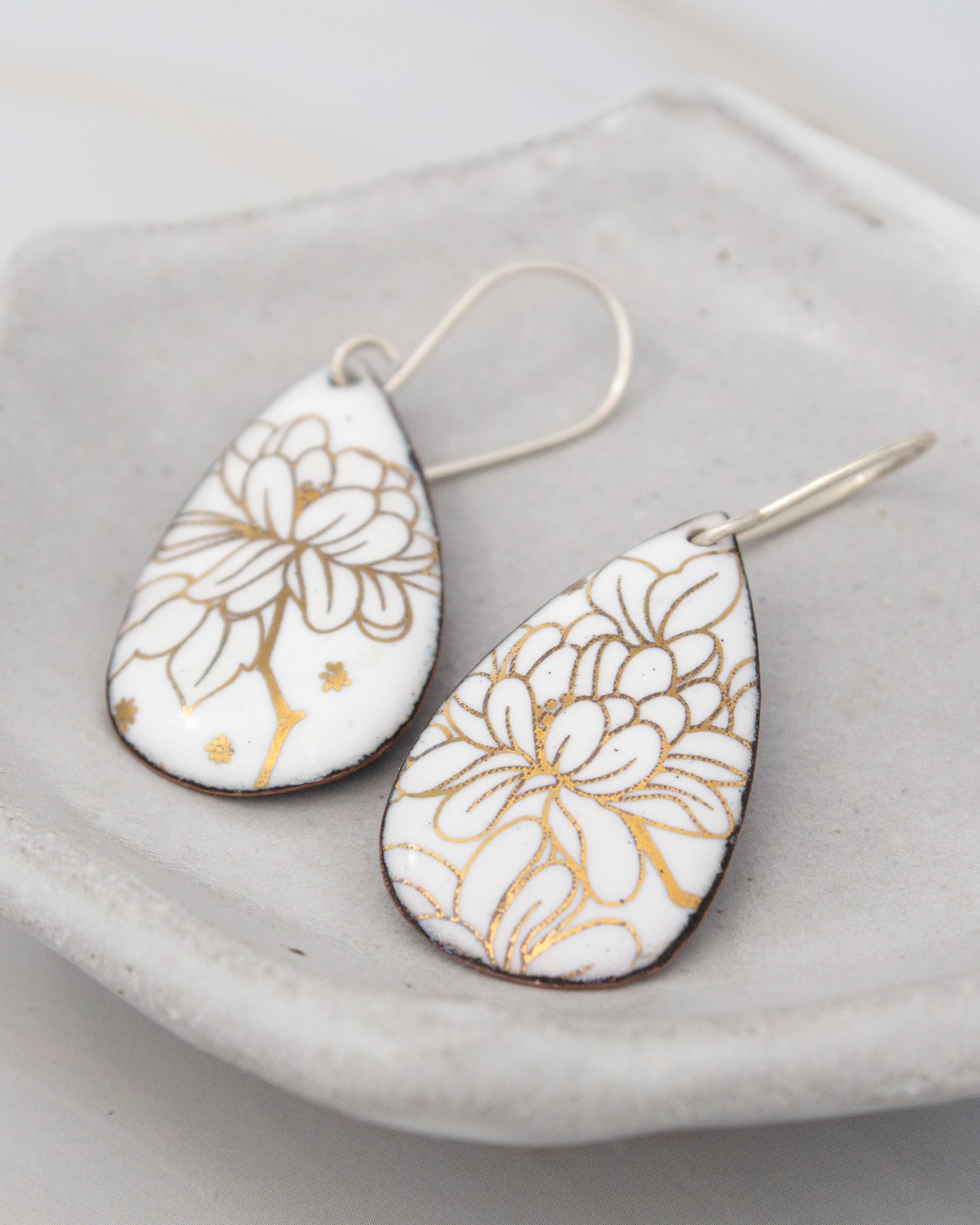 a pair of white earrings with gold floral designs, resting on a white surface.
