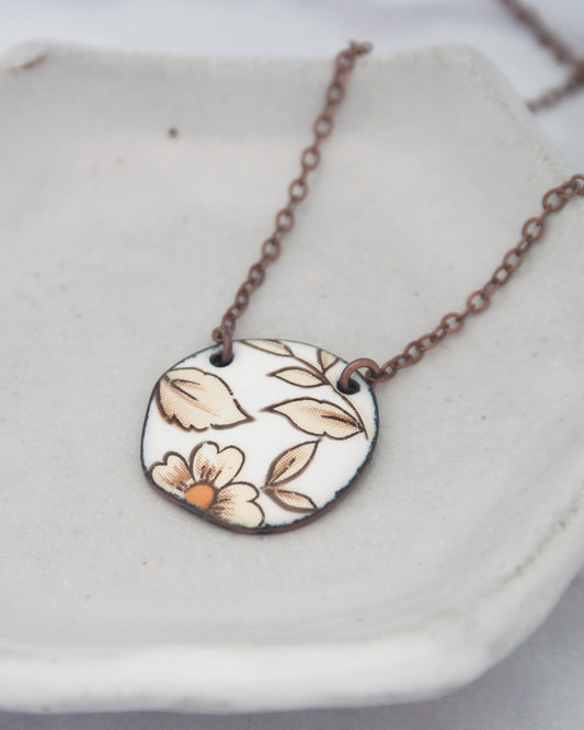 A necklace with a circular pendant featuring a floral design in brown and white colors.
