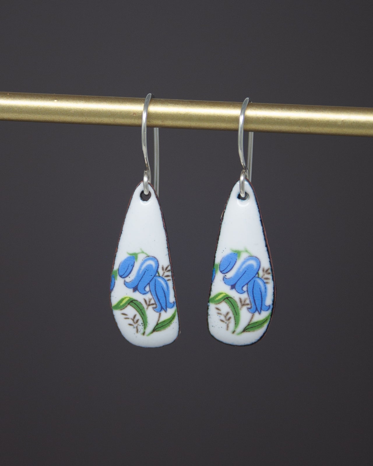 A pair of earrings with blue floral designs hanging from a gold-colored metal hook.