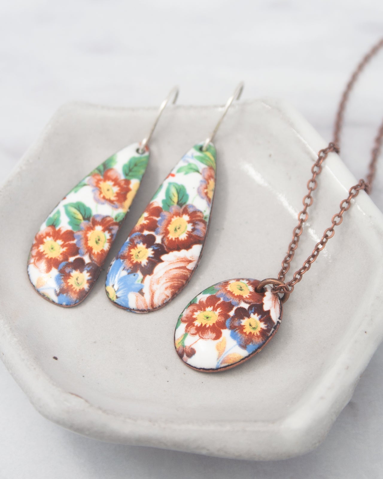 A pair of earrings and a necklace with floral designs are displayed on a white plate.