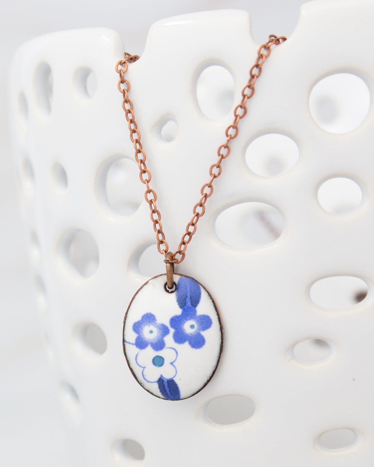 A necklace with a pendant featuring blue flowers is displayed against a white background.