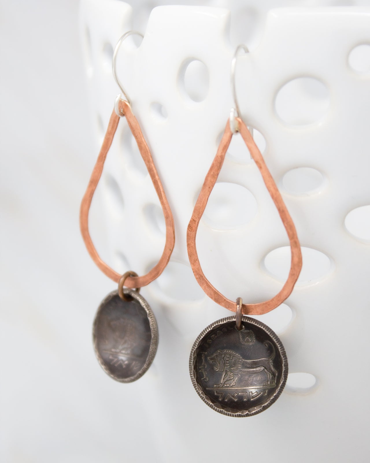 A pair of earrings with a metal lion design on the circular pendant, hanging from a copper-colored metal frame.