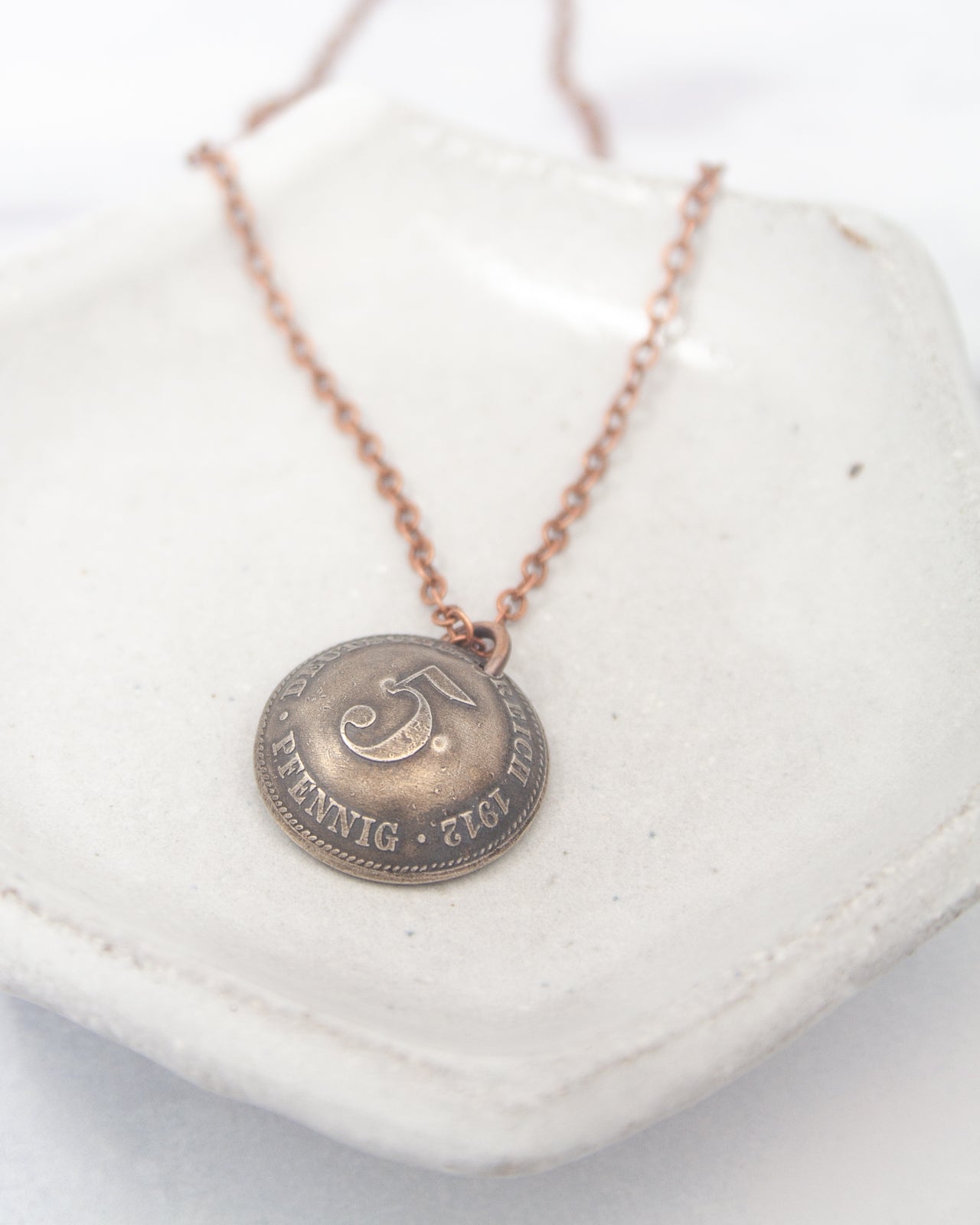 A silver-colored pendant necklace with a circular pendant featuring a symbol and text.