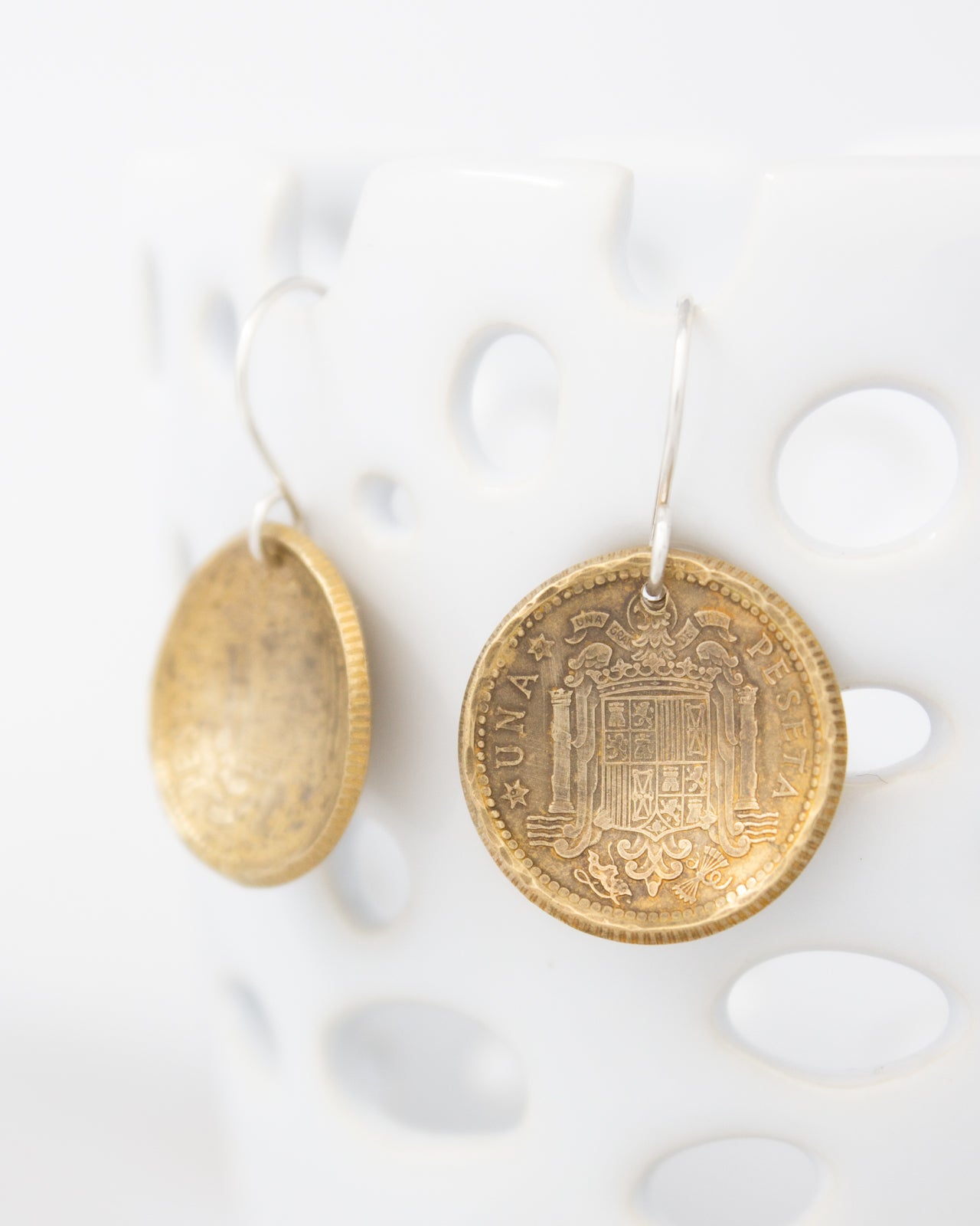 two gold-colored earrings hanging on a white surface.