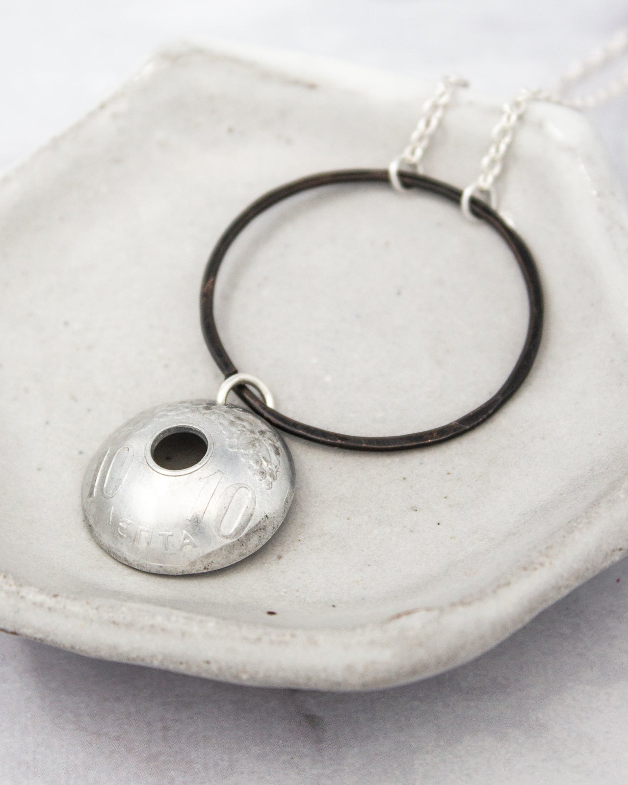 A silver necklace with a pendant featuring the number "10" and the word "SILVER" engraved on it, resting on a white surface.