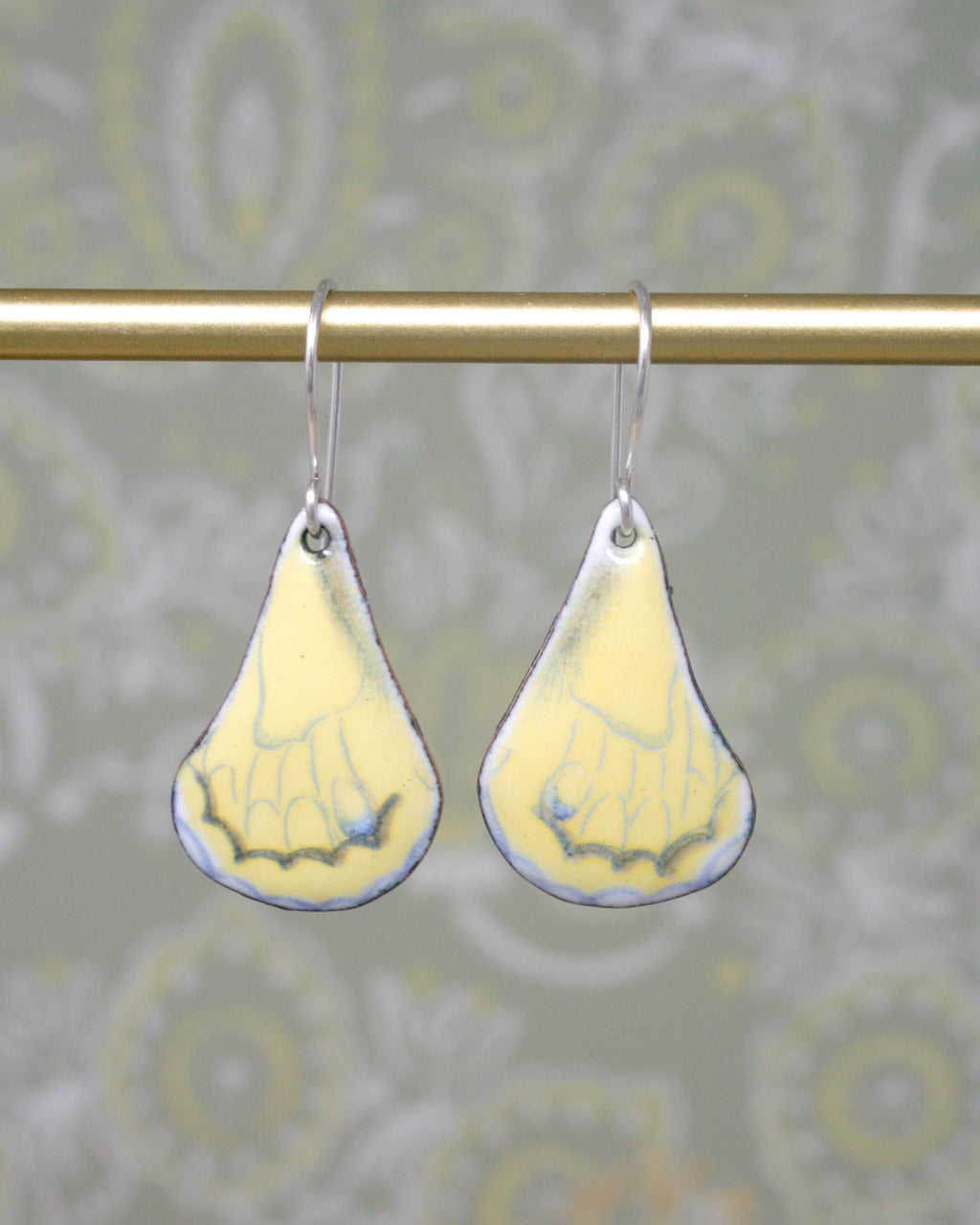 a pair of yellow and white earrings hanging from a metal rod