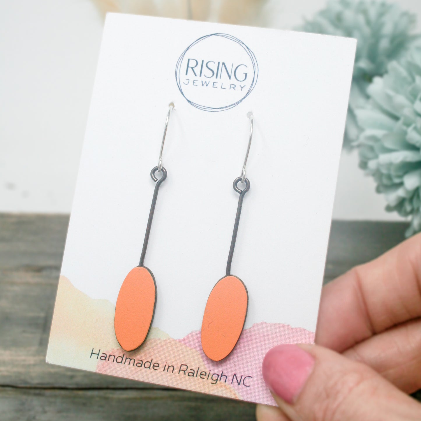 a hand holding a pair of orange earrings