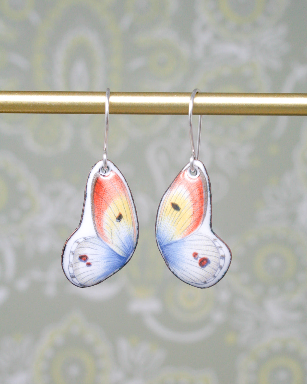 A pair of colorful butterfly earrings hanging from a gold bar.