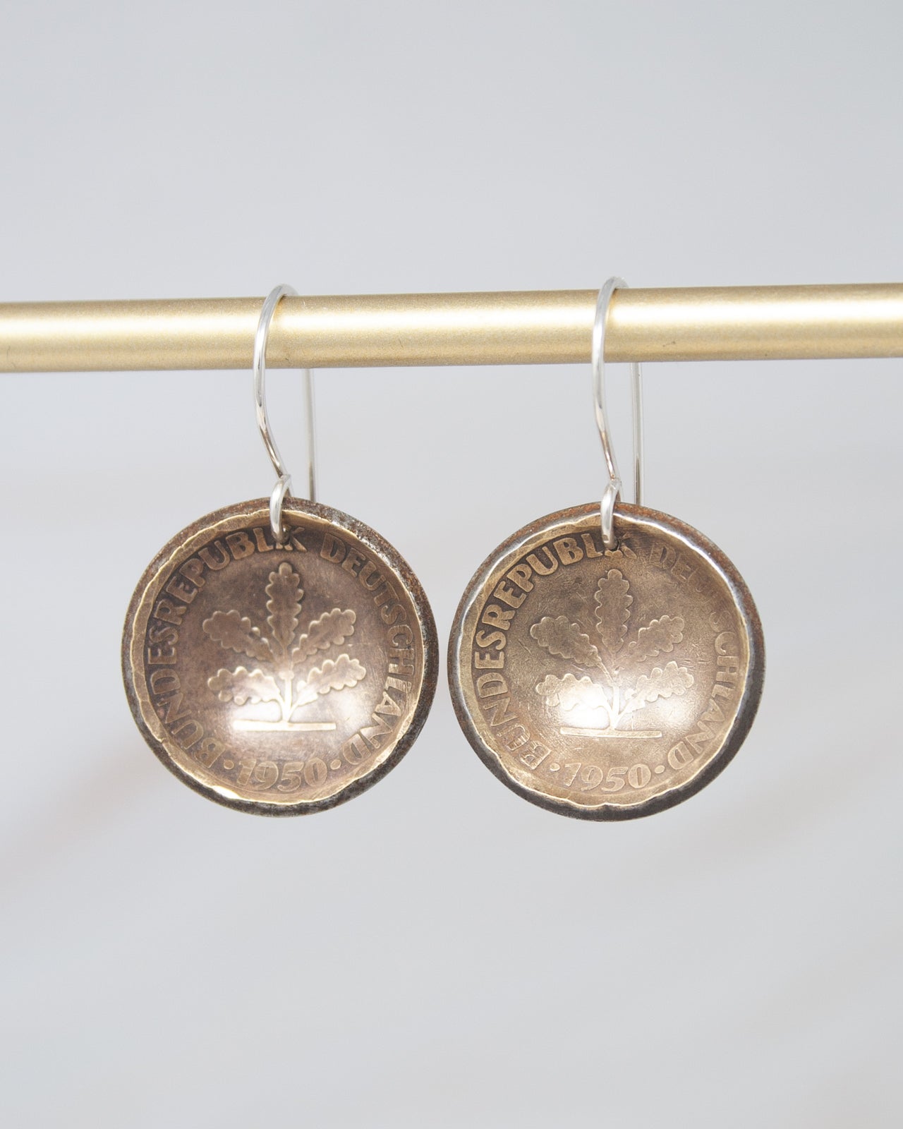 A pair of earrings made from two old coins, hanging from a gold-colored metal hook.