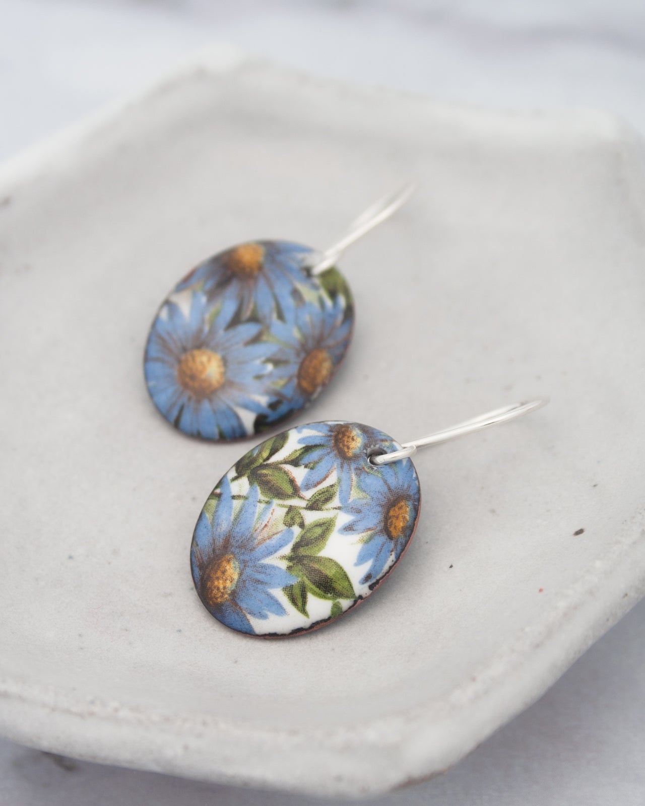 a pair of earrings with blue floral designs on a white plate.