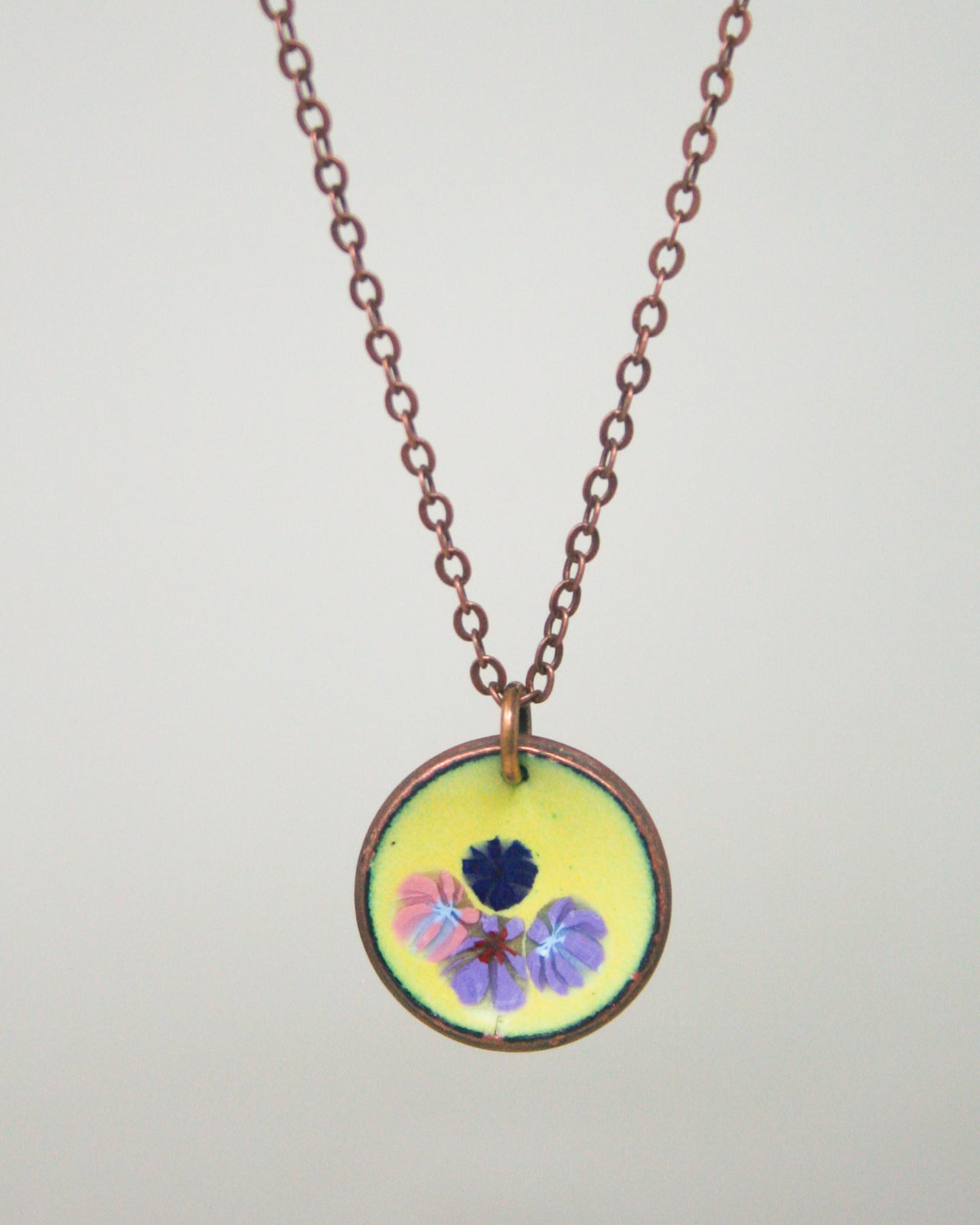 A round pendant necklace with a floral design on a yellow background.