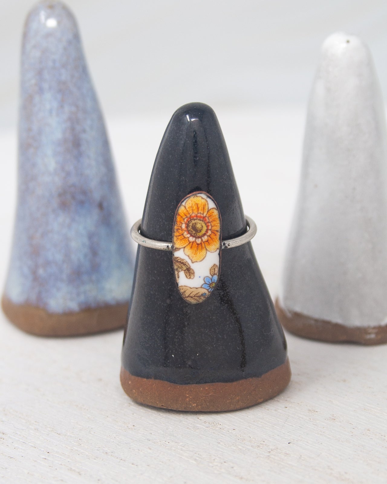 A black ceramic ring stand with a floral design on it, placed between two white ceramic objects.