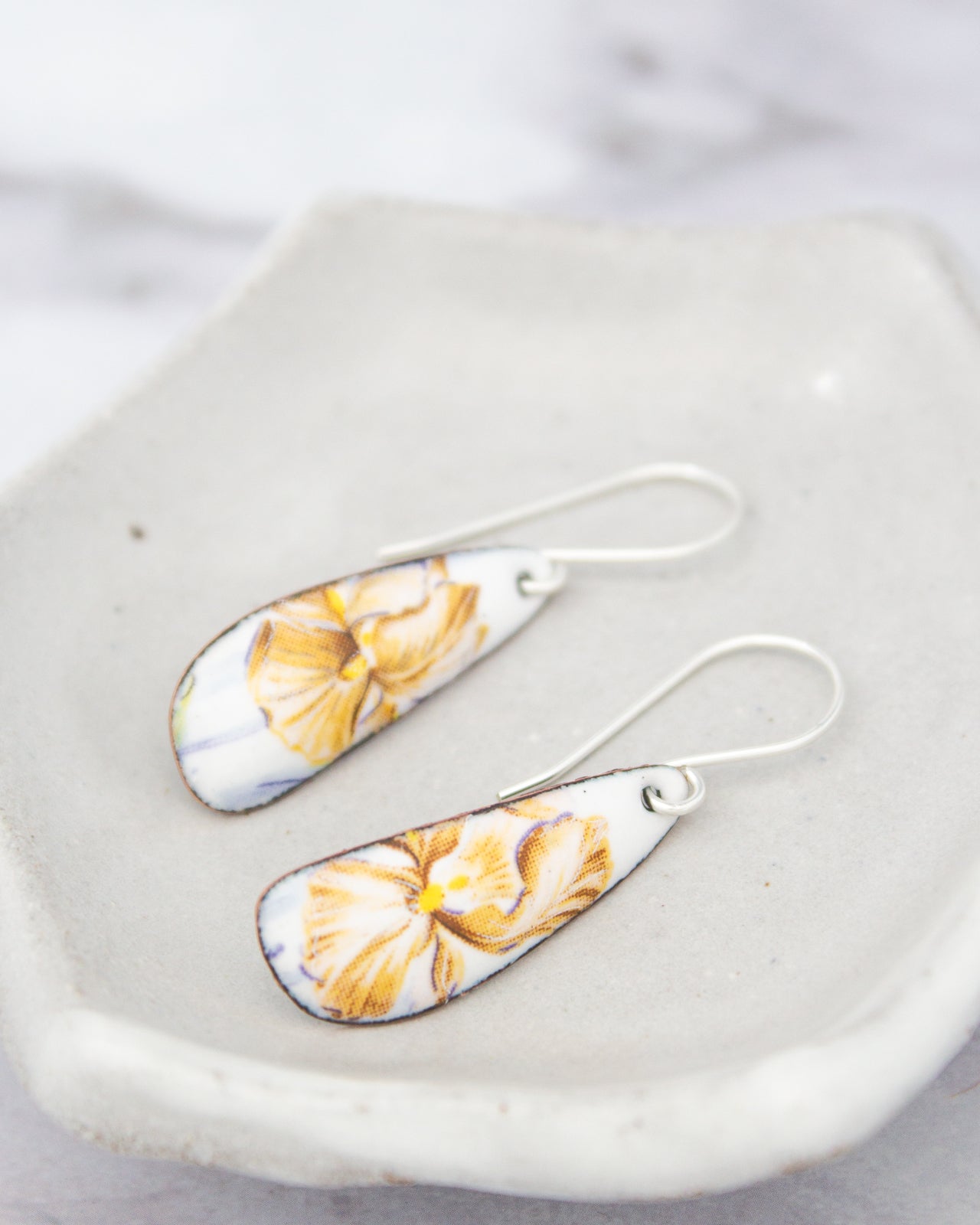A pair of white earrings with yellow floral designs on them, resting on a white surface.
