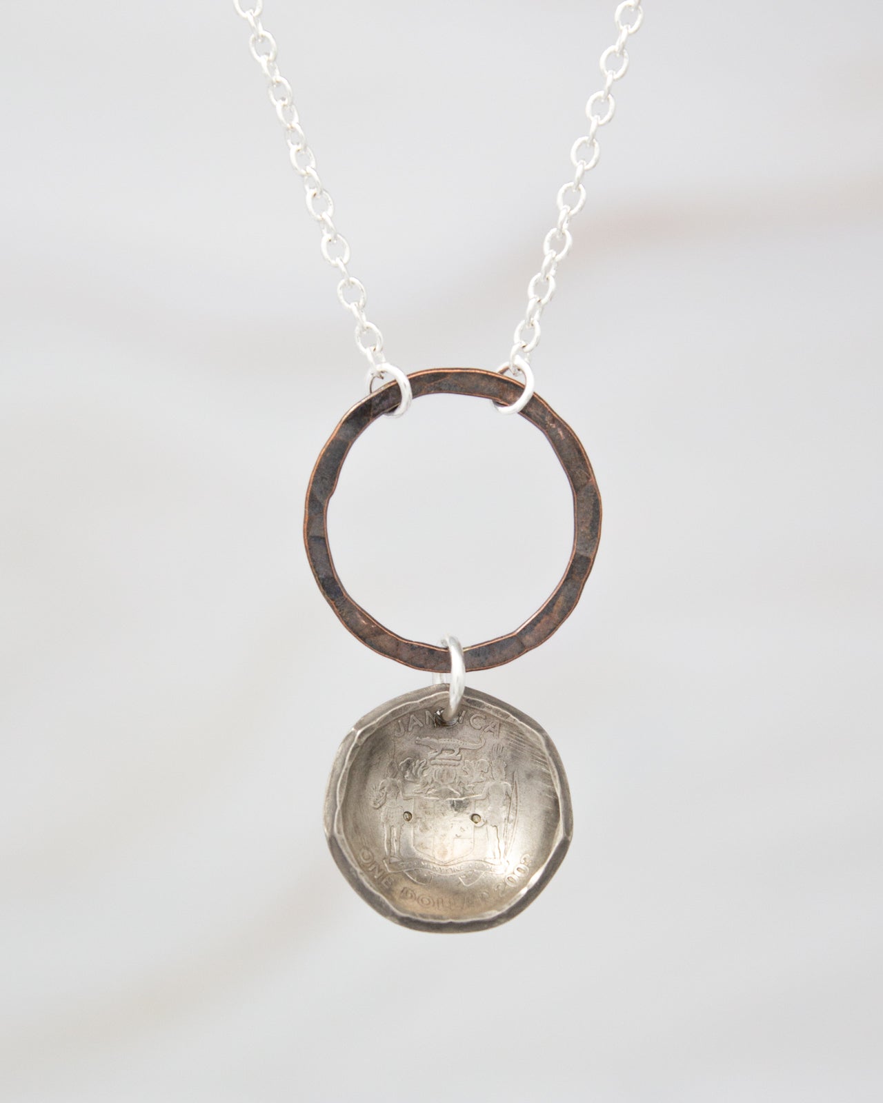 A silver necklace with a round pendant featuring a design, hanging from a chain.