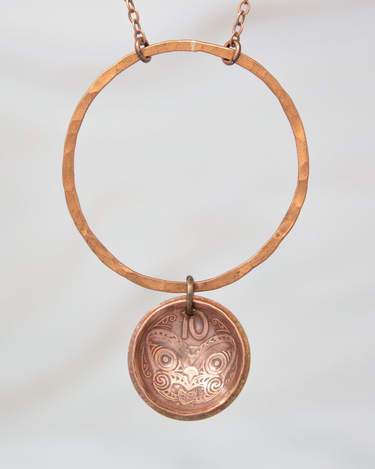 A copper-colored necklace with a circular pendant featuring an intricate design.