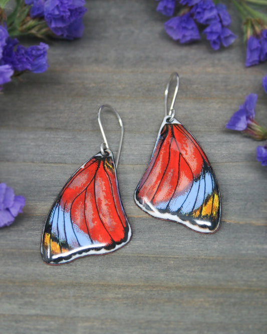 a pair of butterfly shaped earrings sitting on top of a wooden table