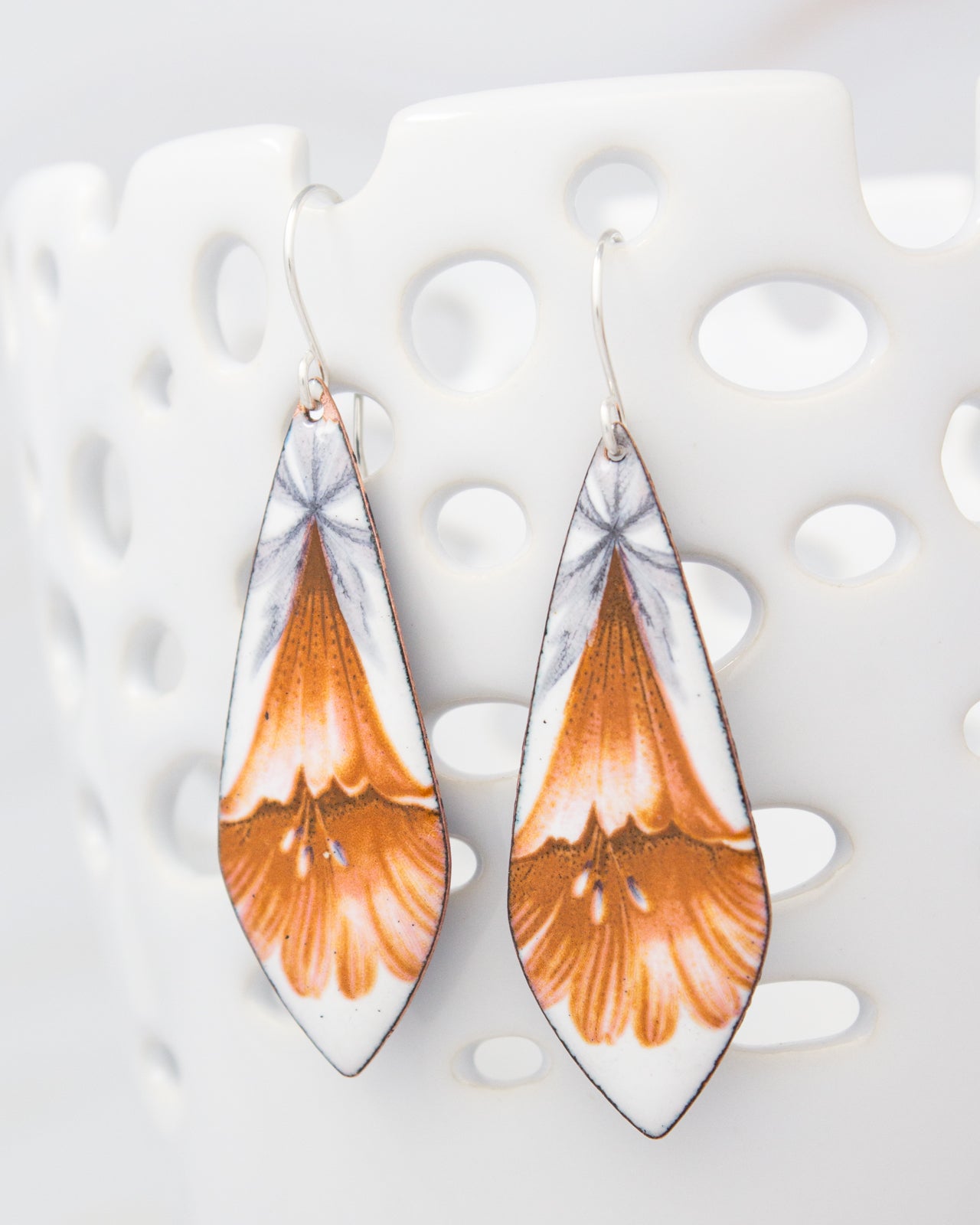 A pair of earrings with a floral design, featuring orange and white colors.
