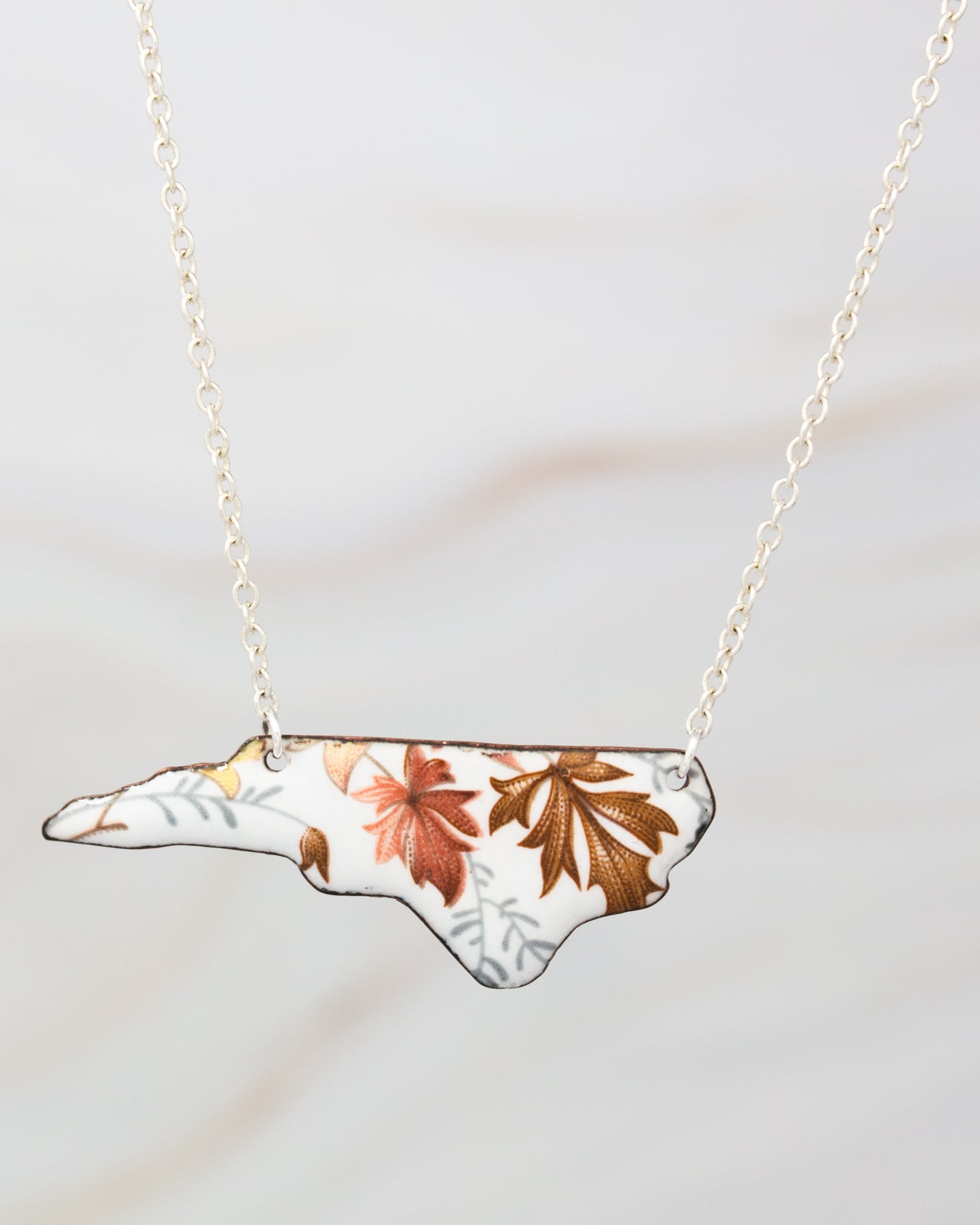 A necklace with a pendant in the shape of the state of North Carolina, featuring a floral pattern in shades of brown and orange.