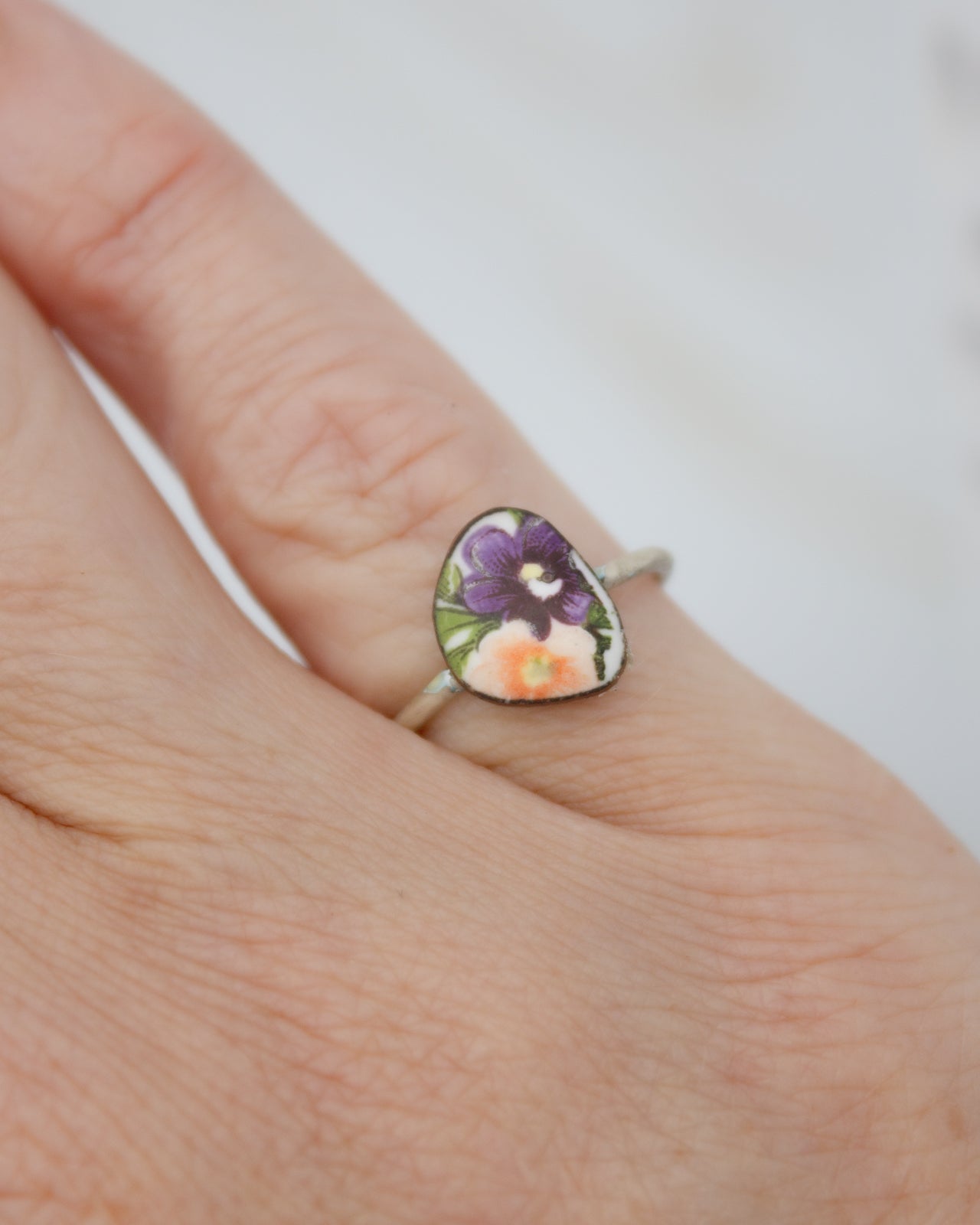 A close-up image of a person's hand wearing a ring with a colorful floral design.