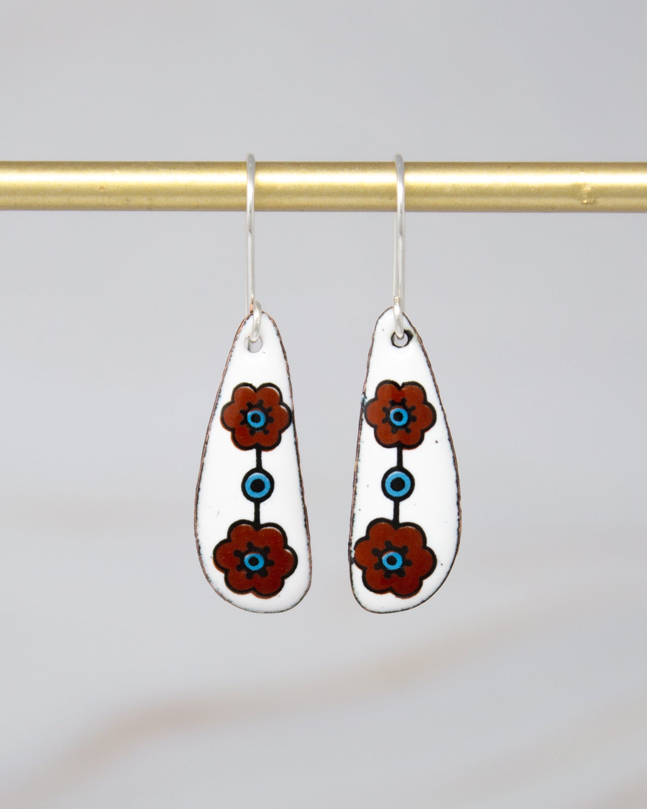 A pair of earrings with white and brown floral designs on a gold bar.