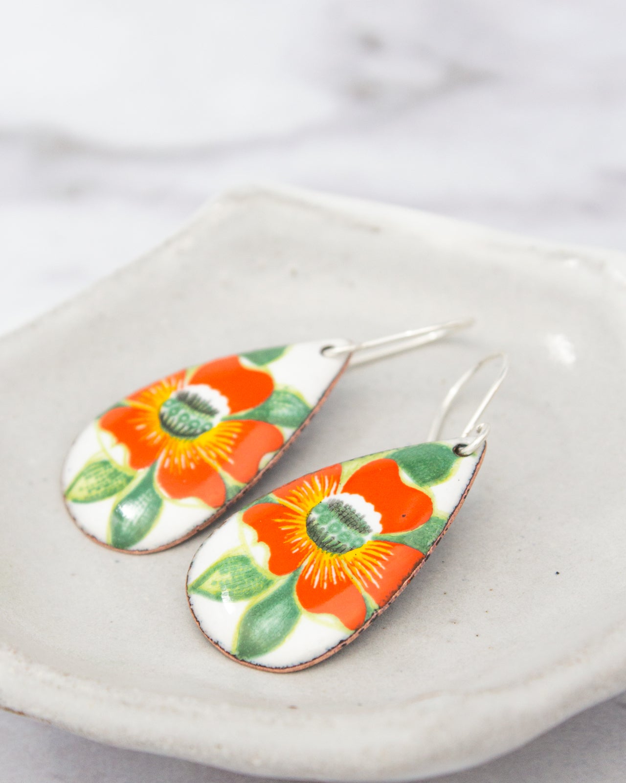 A pair of colorful earrings with orange and green floral designs, resting on a white surface.