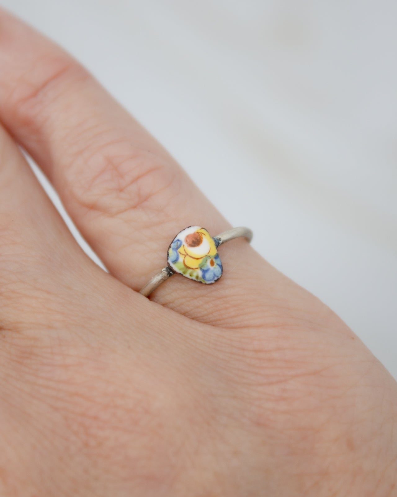 A close-up of a person's hand wearing a ring with a colorful, floral-patterned stone.