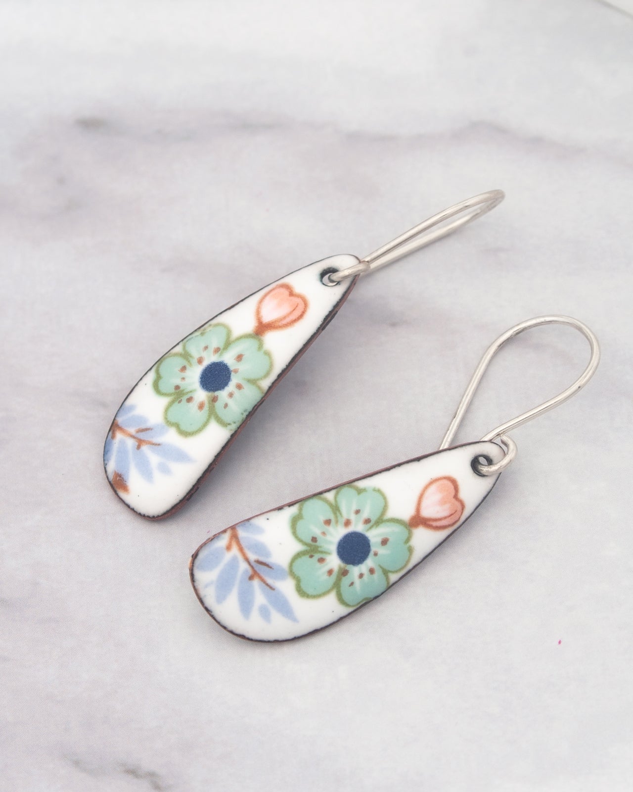 A pair of earrings with colorful floral designs on their surfaces, resting on a marble surface.