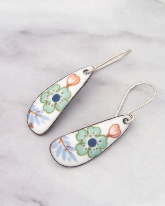 A pair of earrings with colorful floral designs on their surfaces, resting on a marble surface.