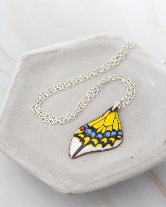 A necklace with a pendant featuring a colorful butterfly design rests on a white plate.