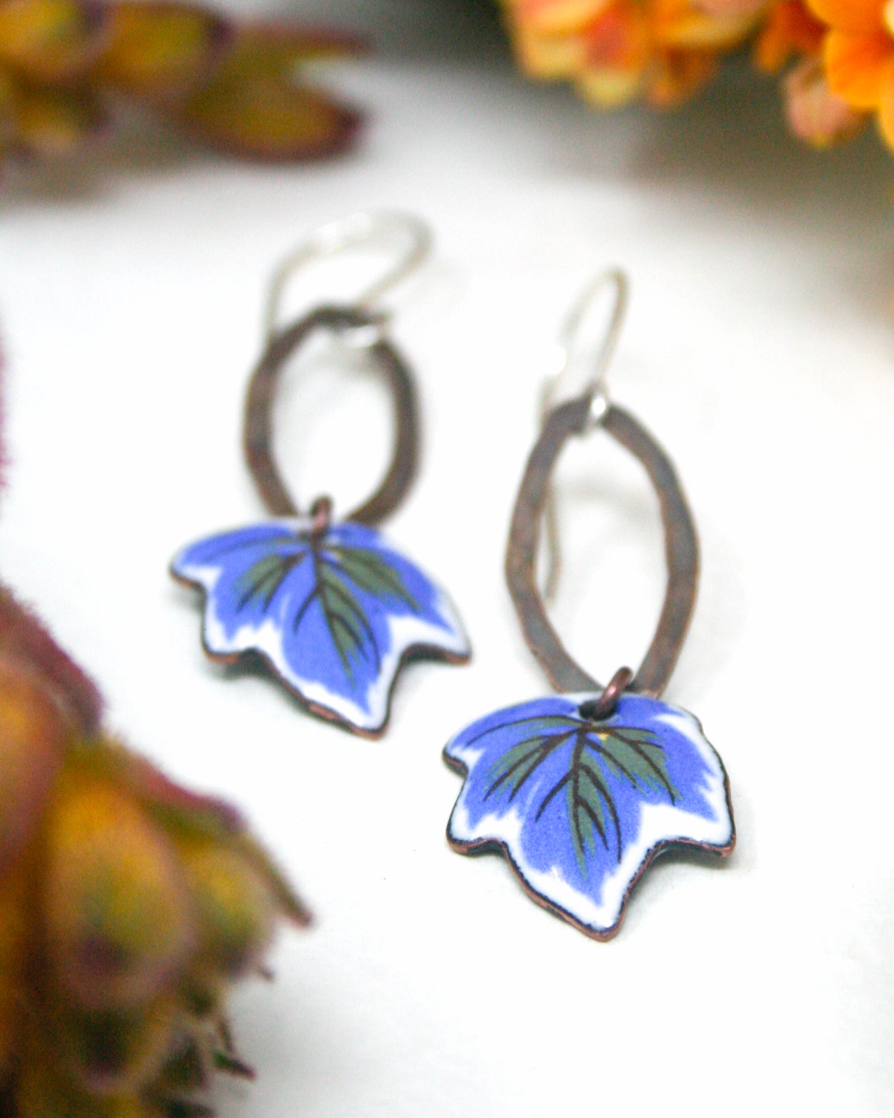 A pair of earrings with blue leaf-shaped designs, featuring a combination of metallic and painted elements.