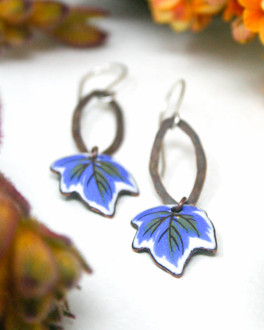 A pair of earrings with blue leaf-shaped designs, featuring a combination of metallic and painted elements.