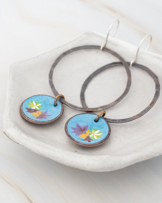 A pair of earrings with blue enamel and floral designs, displayed on a white plate.