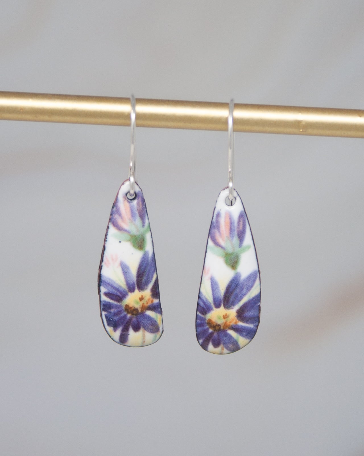 A pair of earrings with a floral design hanging from a gold bar.