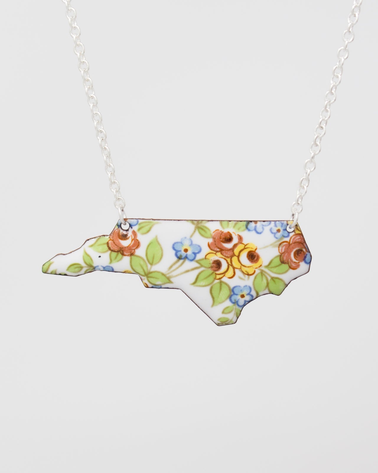 A necklace with a pendant in the shape of the state of North Carolina, decorated with colorful floral patterns.